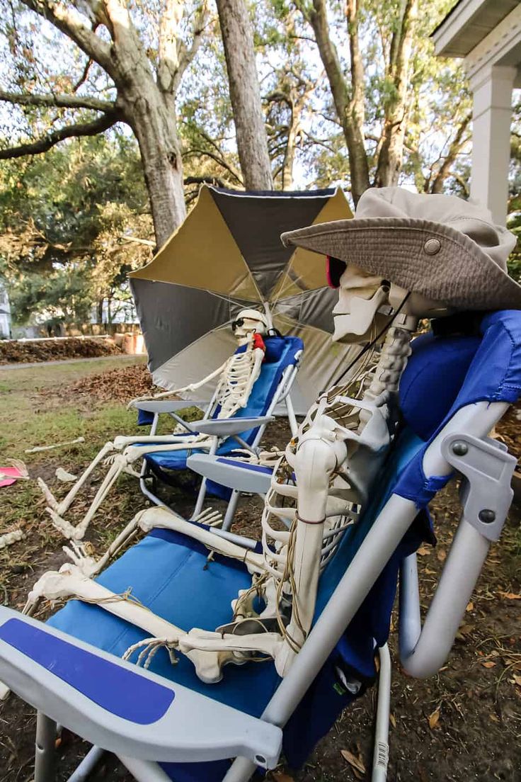 two lawn chairs with hats and umbrellas on them sitting in front of a house