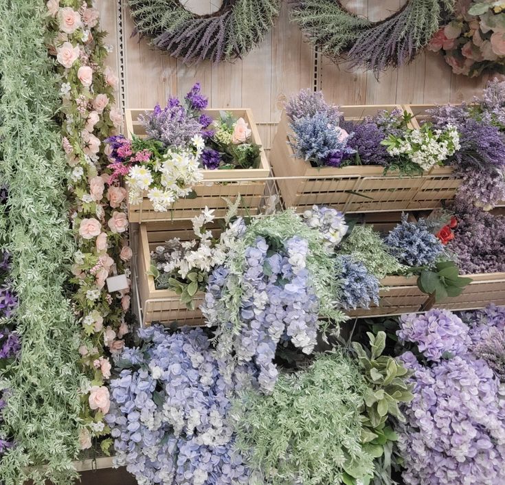 many different types of flowers on display in wooden crates and baskets with wreaths above them