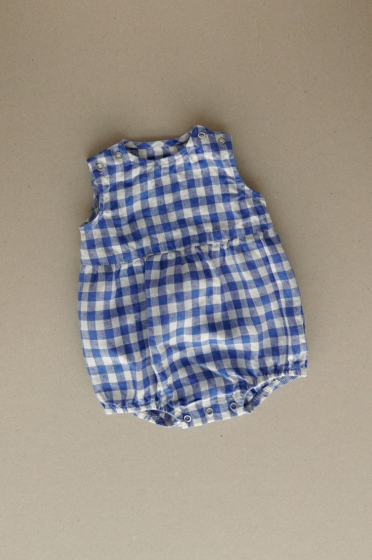 Product photos - blue gingham. The model is wearing a romper in yellow gingham. All-day comfort is guaranteed with this sleeveless romper crafted from medium-weight linen. The fabric is soft, breathable, and light on the skin. For simple changing, the romper is designed with popper snap fastenings on the shoulders and bottom. The waist seam in the middle adds a nice final touch to an adorable silhouette, and elasticated leg cuffs secure the romper in place. This baby romper is designed to be comfortably loose-fitting and allow for growth as the baby grows. Plaid Cotton Bubble Romper For Summer, Summer Cotton Plaid Bubble Romper, Summer Plaid Cotton Bubble Romper, Cute Gingham Bubble Romper For Spring, Summer Gingham Cotton Bubble Romper, Cute Summer Plaid Bubble Romper, Cute Spring Gingham Bubble Romper, Blue Bubble Romper For Summer, Cute Gingham Cotton Bubble Romper