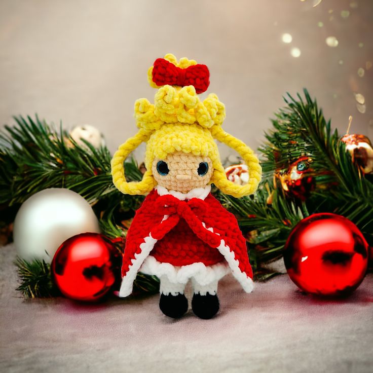 a crocheted doll sitting next to christmas ornaments