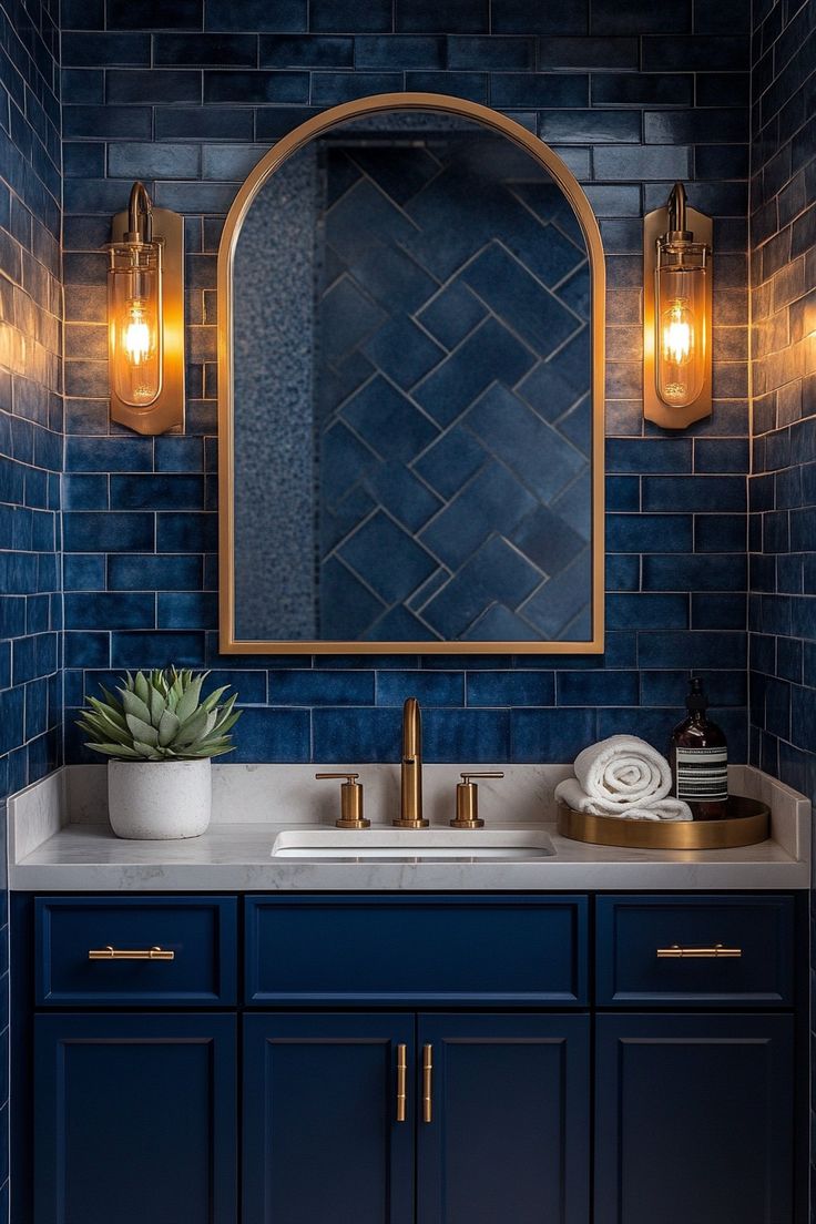 a bathroom with blue tile and gold accents, including a mirror over the sink that has lights on it