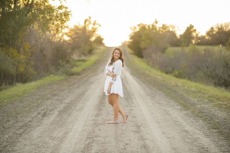 a woman is standing in the middle of a dirt road