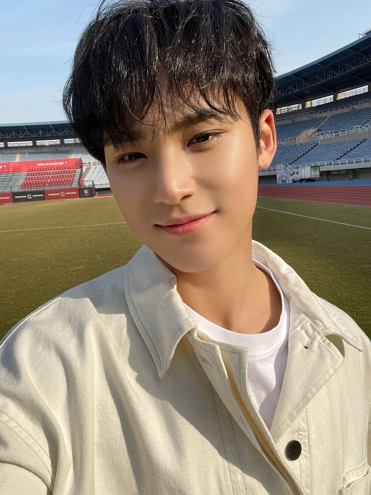 a young man standing in front of an empty soccer field with stadium seats behind him