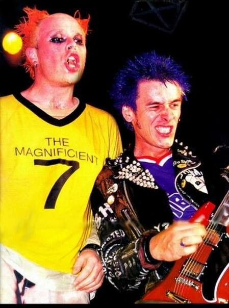 two men with punk hair and makeup are playing guitars