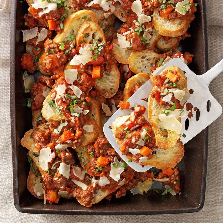 a casserole dish with meat and cheese on top, next to a serving utensil