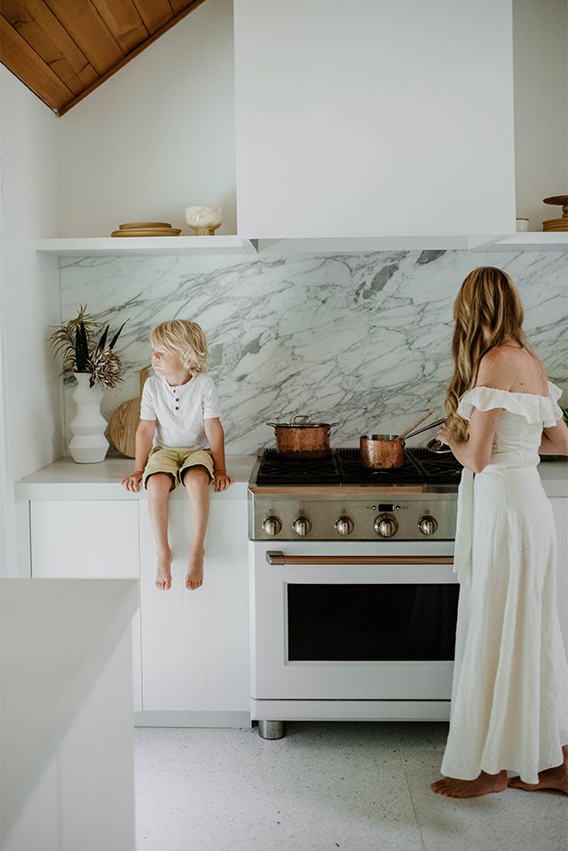 a woman and her child are sitting on the counter in front of an oven with pots