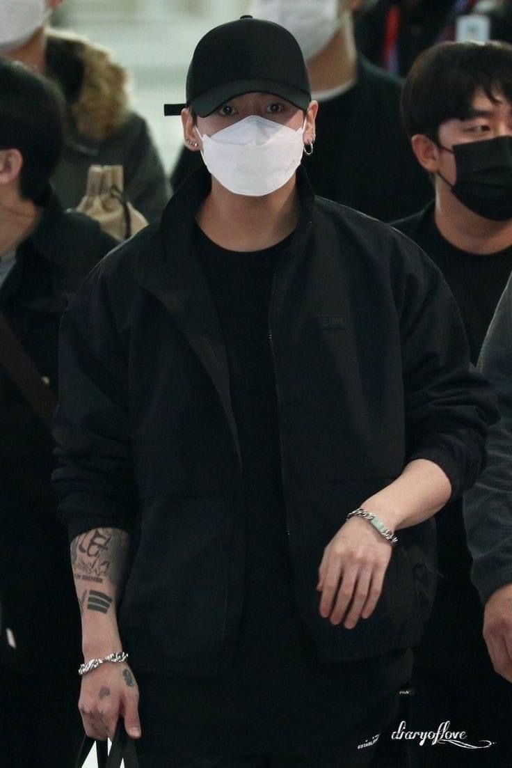 a man wearing a face mask and black jacket is walking through an airport with other people in the background