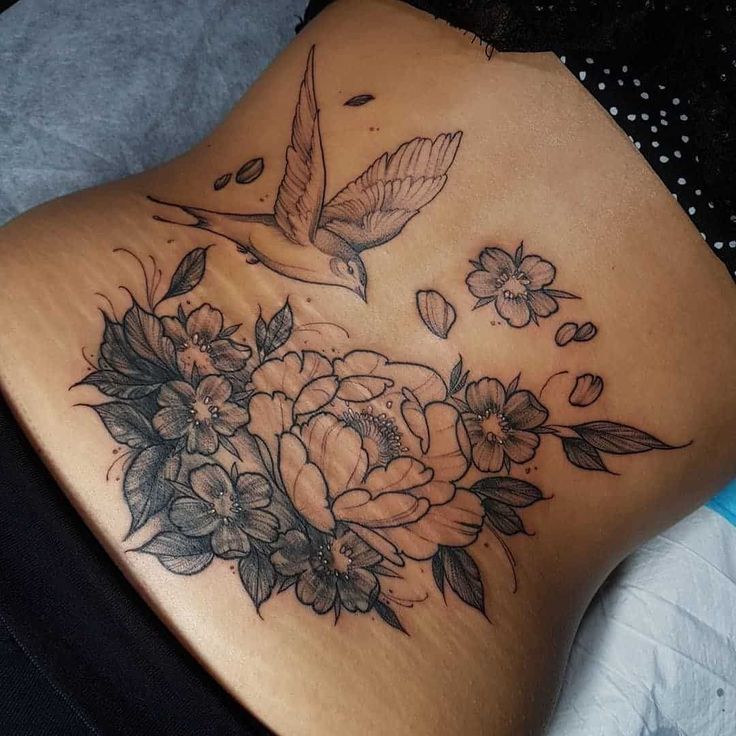 a woman's back with flowers and a bird tattoo on her lower back side