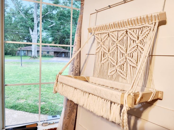 a macrame hanging from the side of a wall next to a window with grass outside