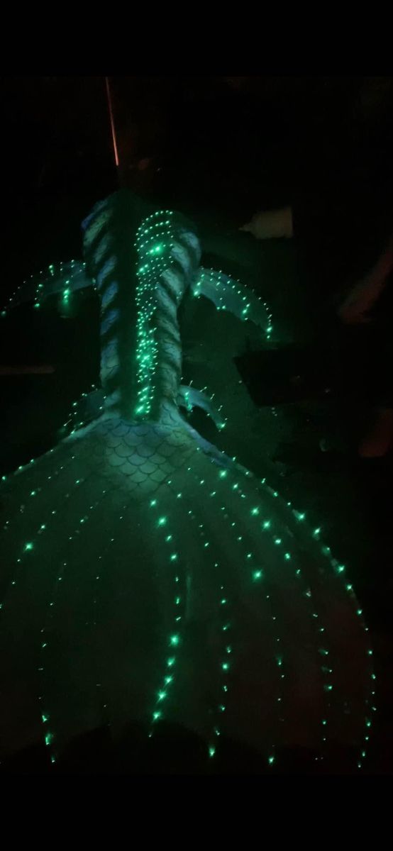 a person in a green dress with lights on their body and arms, walking through the dark