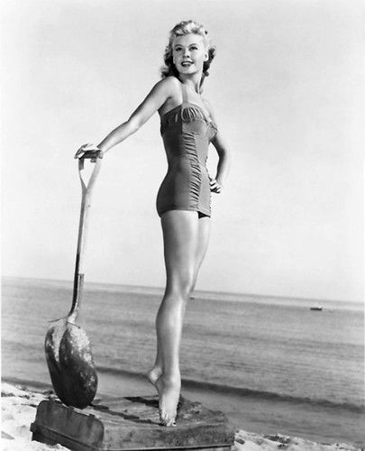 a woman in a bathing suit standing on a rock near the ocean with a paddle