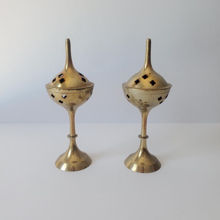 two brass candlesticks sitting side by side on a white surface with one candle holder in the middle