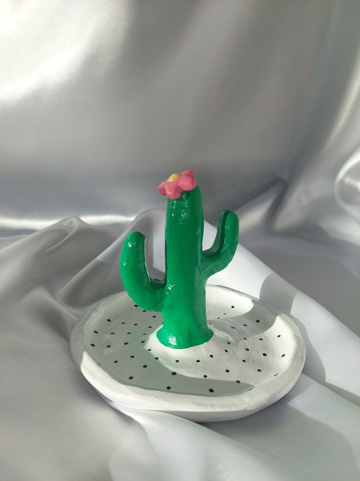 a green cactus with a pink flower sitting on a white plate