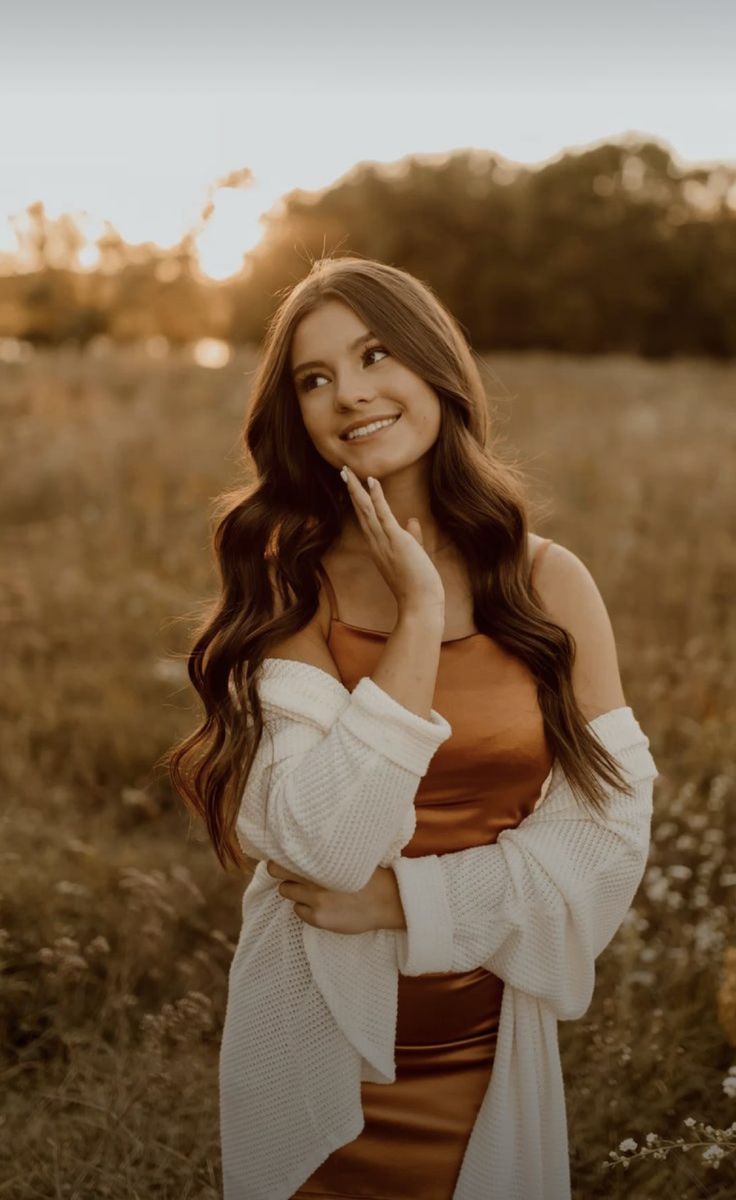 a woman standing in a field with her hands on her face and looking at the camera