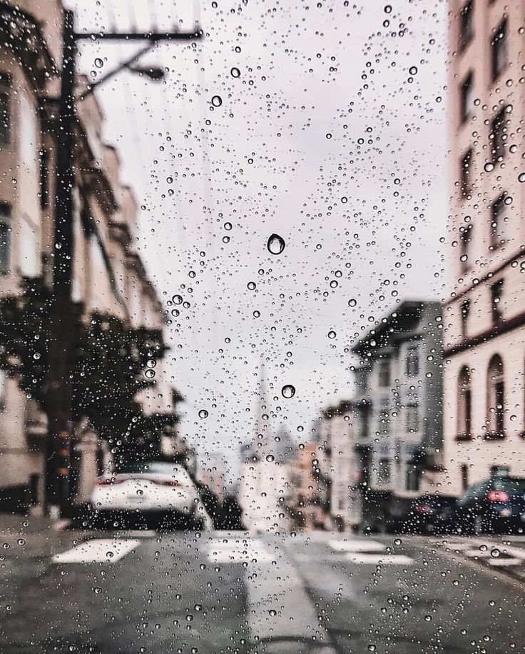 an instagram with rain drops on the window and cars parked in the street behind it