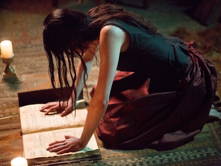 a woman kneeling down on the ground reading a book with lit candles in the background