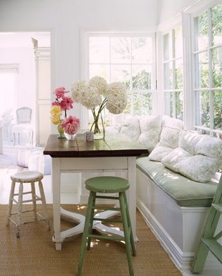 a table with two stools next to a bench and flowers in a vase on it