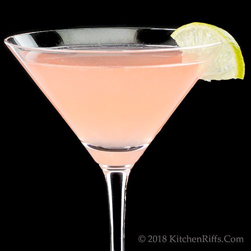 a pink drink with a lime slice on the rim in front of a black background