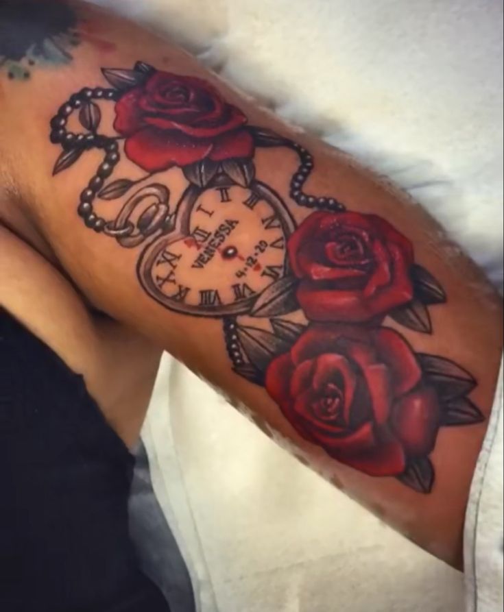 a man's arm with roses and an alarm clock tattoo on it, while he is laying in bed