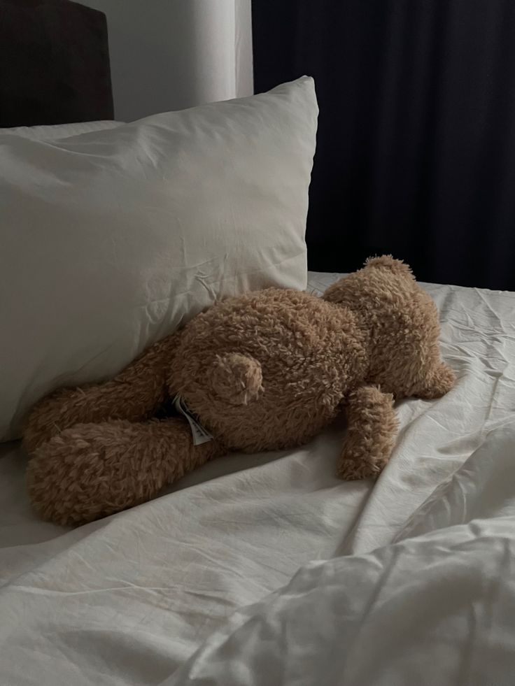 a brown teddy bear laying on top of a white pillow