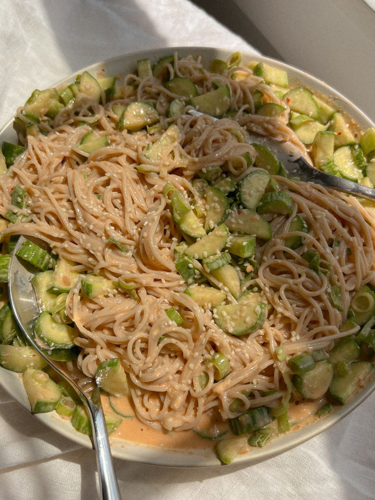 a white plate topped with pasta and veggies on top of a table next to a fork