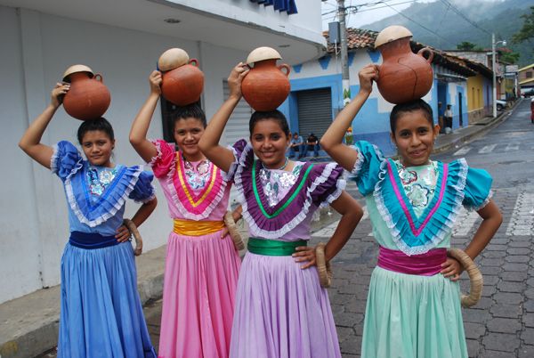 four girls in colorful dresses holding up pots on their heads