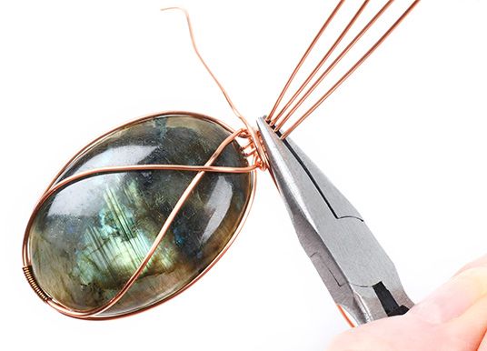 a person is cutting wire with a pair of scissors and a large labradorite stone