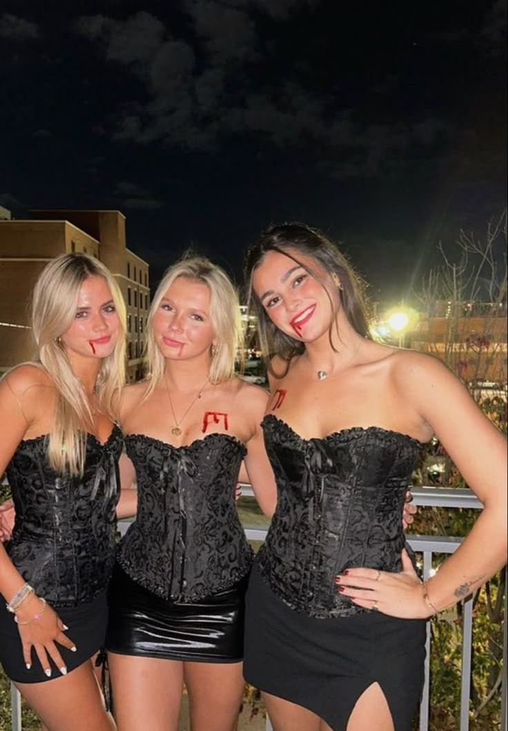 three beautiful young women standing next to each other in short skirts and black corsets