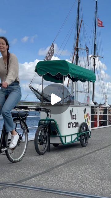 a woman riding a bike next to a small ice cream cart on top of a pier