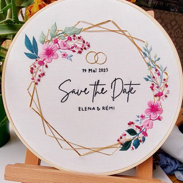 a white embroidered wedding sign with pink flowers and greenery in the center on a wooden easel