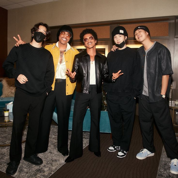 four young men standing next to each other in a living room with one man wearing a mask