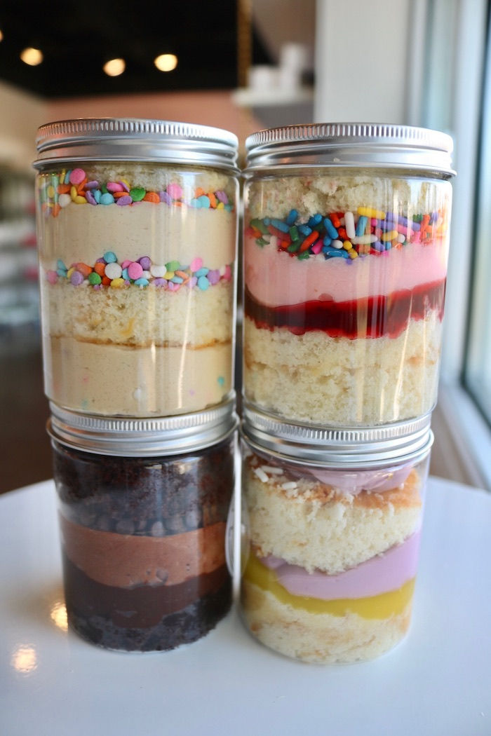 three jars filled with different types of desserts on top of a white table next to a window