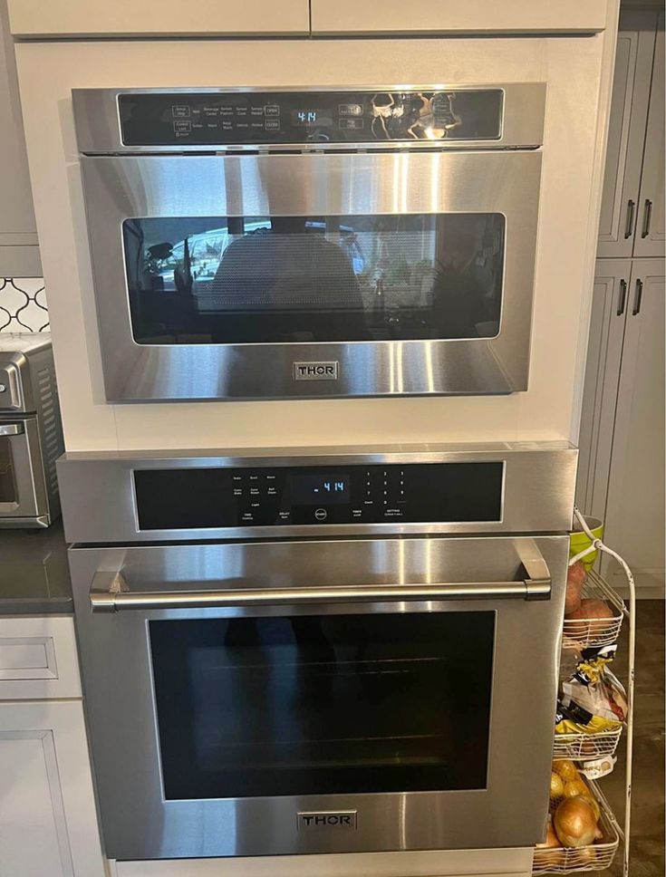 two ovens side by side in a kitchen with stainless steel appliances and white cabinets