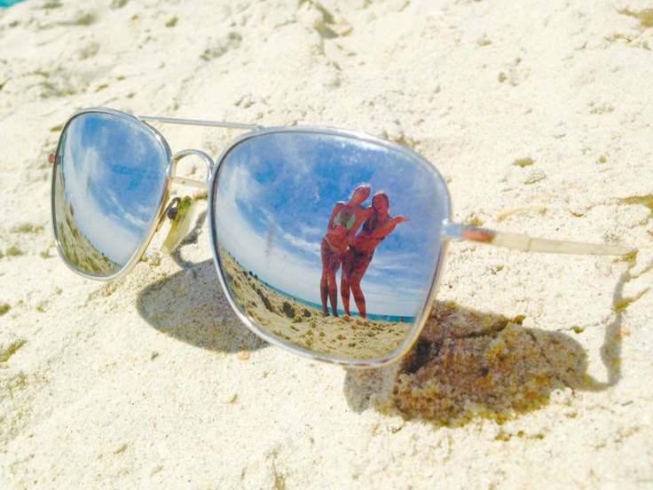 the reflection of two people in their sunglasses on the sand