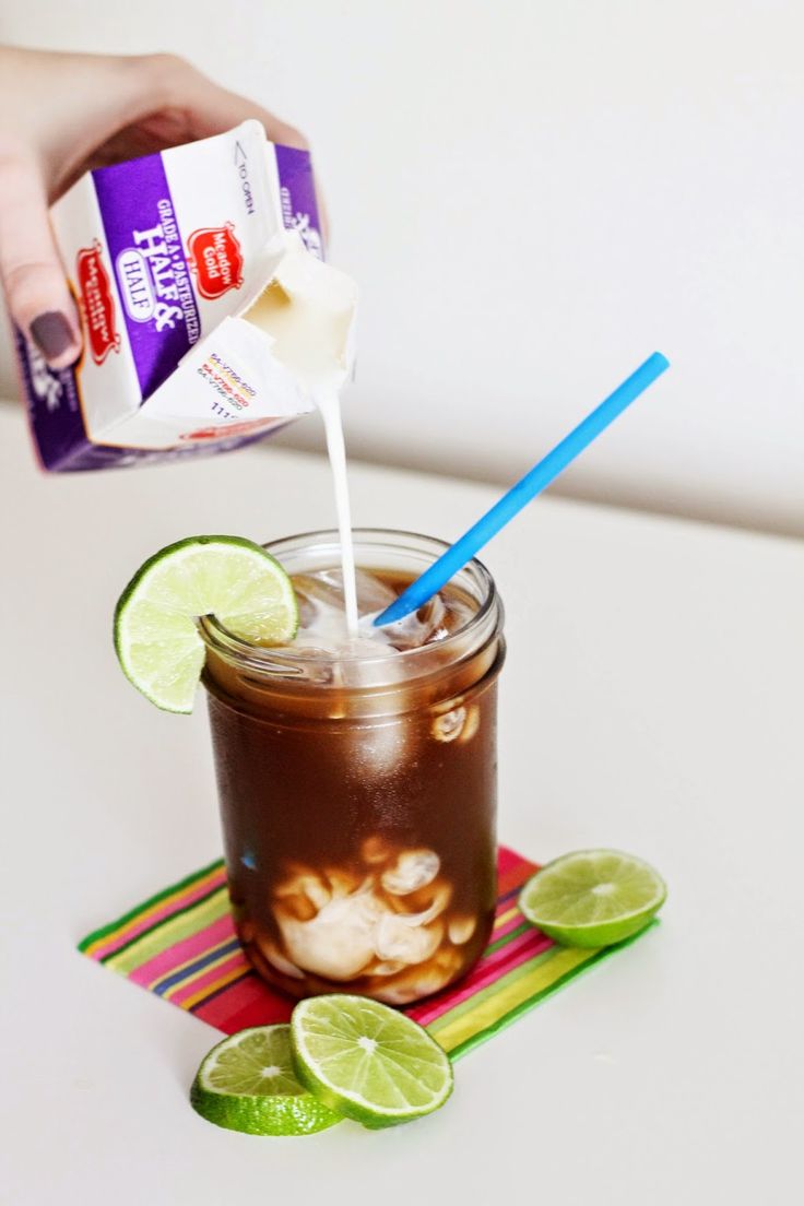 a person pouring milk into a mason jar filled with iced coffee and lime wedges