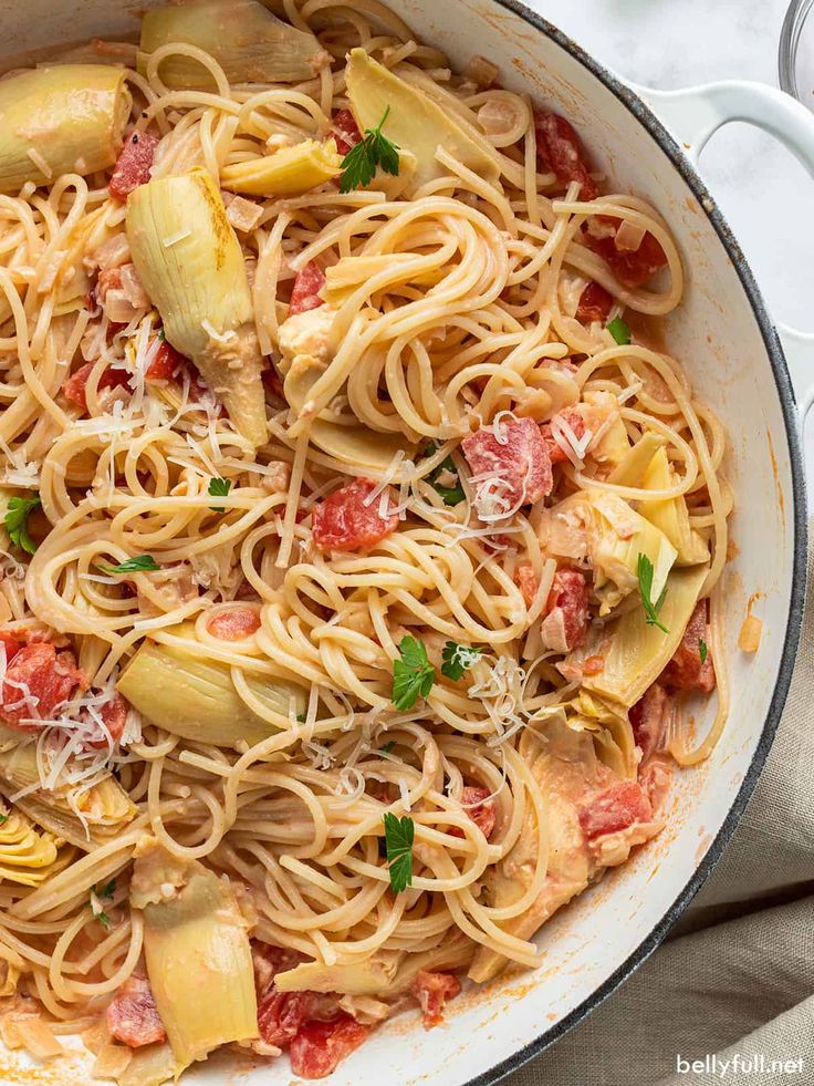 a pan filled with pasta and vegetables on top of a white table cloth next to utensils