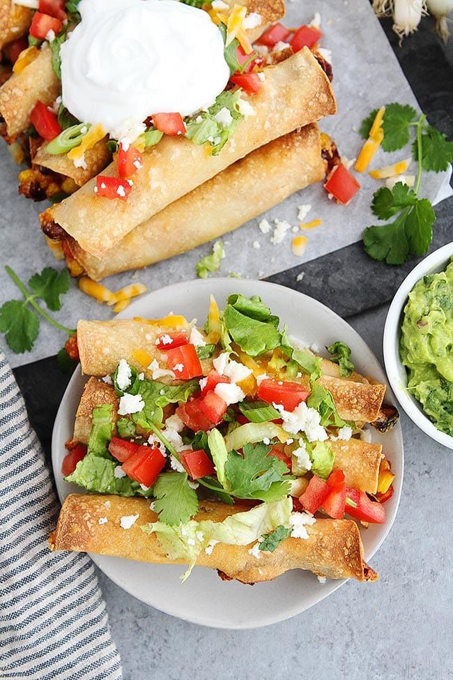 two burritos on plates with guacamole, salsa and sour cream