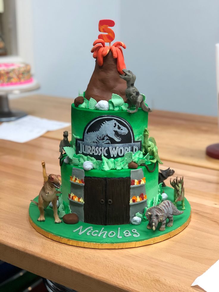 a green cake with dinosaurs on it sitting on a table