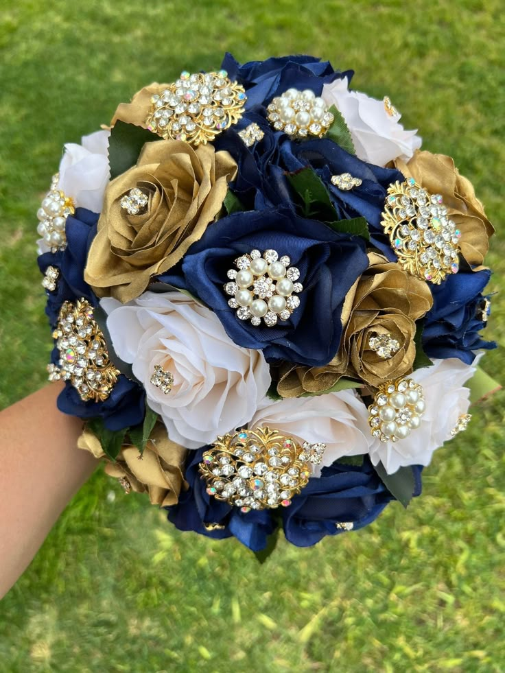 a bridal bouquet with blue, white and gold flowers on the grass in front of someone's hand