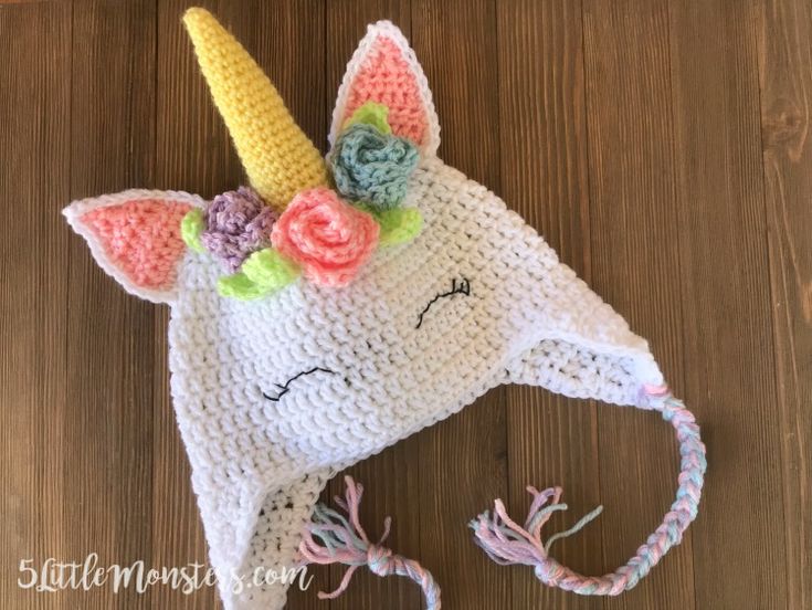 a crocheted unicorn hat with flowers on it's head sitting on top of a wooden floor