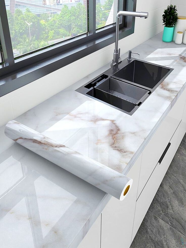 a kitchen with marble counter tops and white cupboards in front of a large window