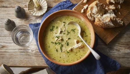 a bowl of soup on top of a wooden table next to bread and glass of water