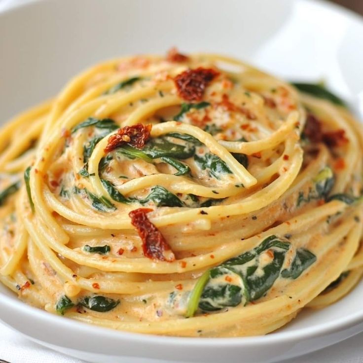 a white bowl filled with pasta and spinach