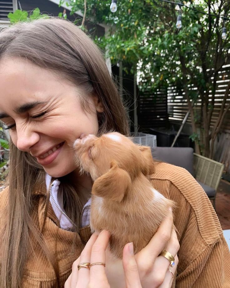 a woman holding a small brown and white puppy in her arms while smiling at the camera