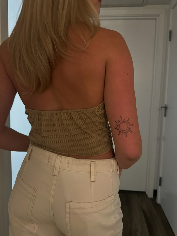 a woman with a tattoo on her back standing in front of a door wearing white pants