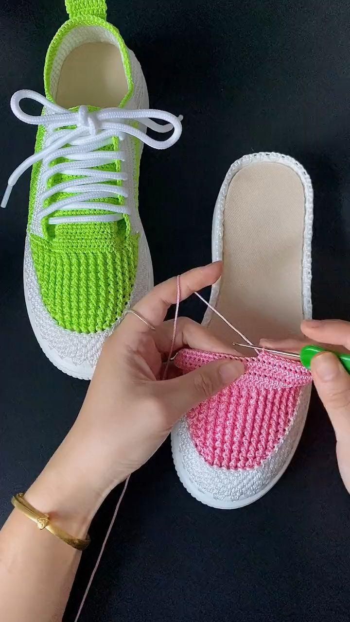 a person is knitting with green and pink yarn on top of a pair of shoes