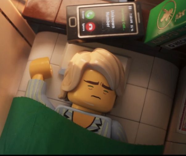 a lego man laying on top of a counter next to a cell phone and remote control