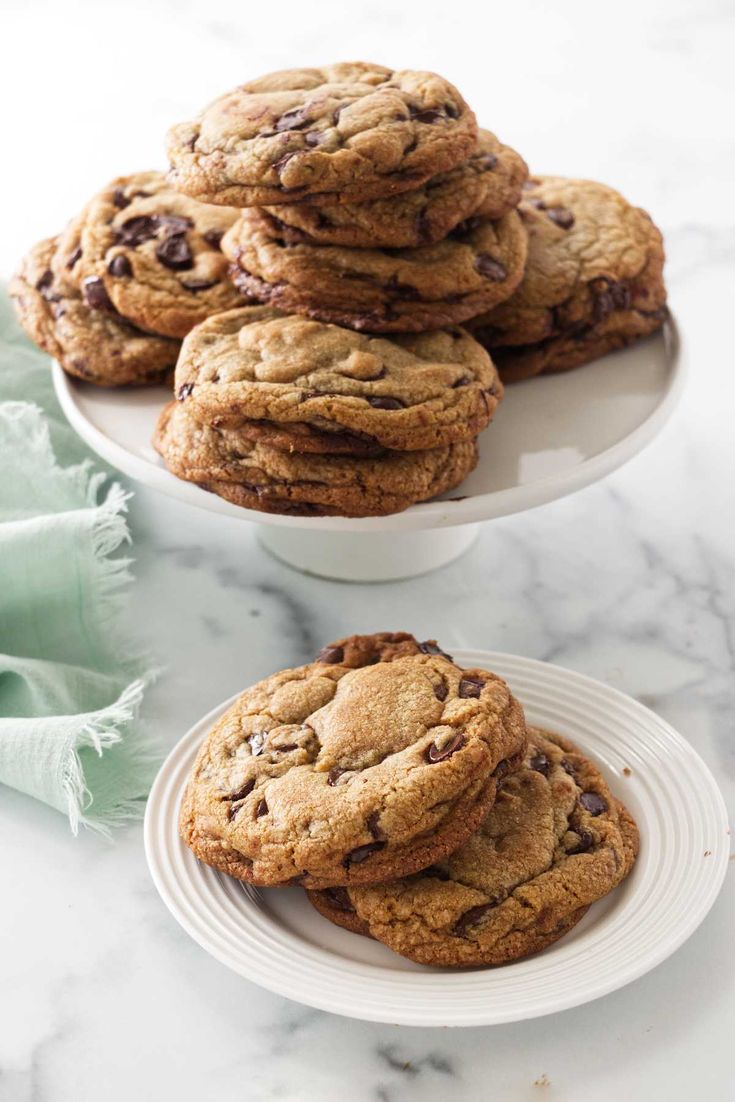 chocolate chip cookies stacked on top of each other in two white plates with green napkins