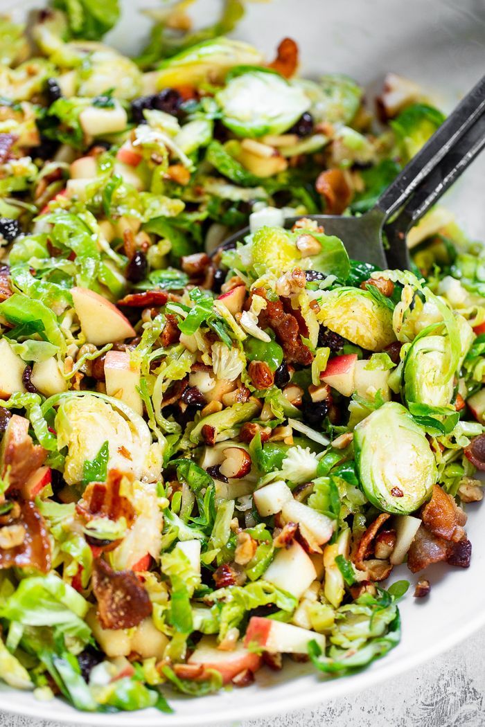 a salad with brussels sprouts, bacon, and other toppings in a white bowl