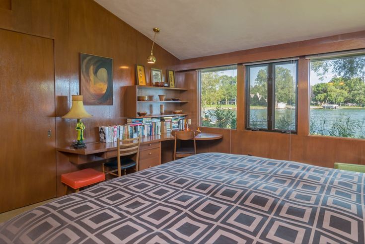 a bedroom with a bed, desk and bookcases in front of large windows